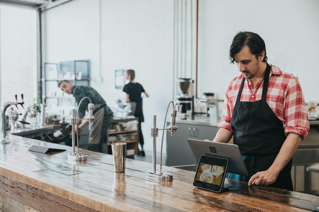 A barista ringing in an order on a Square Register at a cafe counter